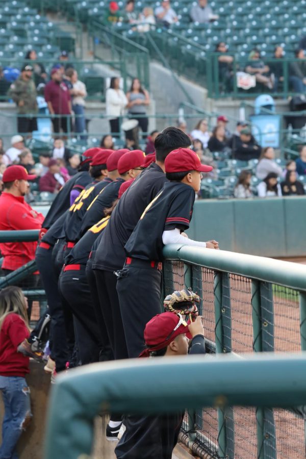 The team enjoys hanging on the rails of the pro dugout at San Manuel stadium as they watch their team on the field.