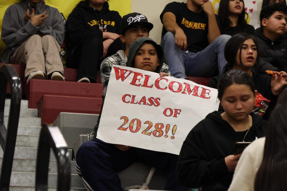 While ASB gets the pep rally going, a middle schooler holds up a sign showcasing his graduating year. 