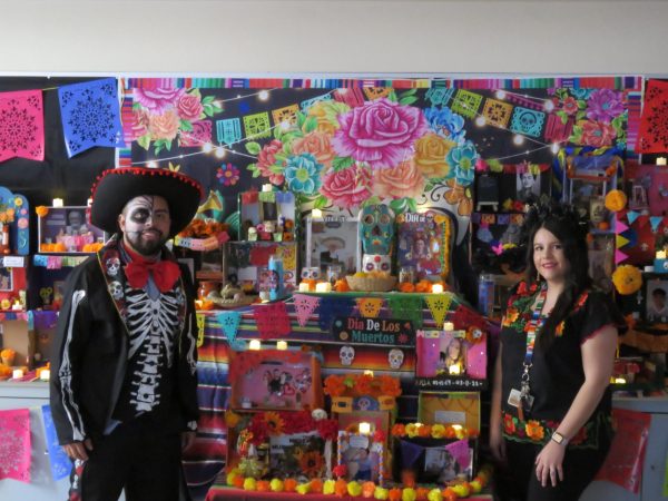 Spanish teachers Evelyn Lopez and Joe Perez stand together In Front of their students ofrendas